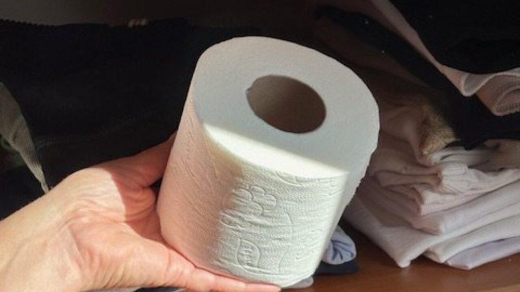 Rolka toaletného papiera položená na poličke s oblečením.