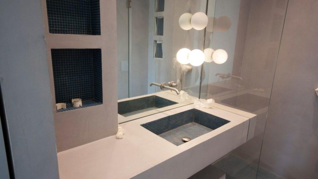 Moderná kúpeľňa so sivým mikrocementom na stenách a umývadle, elegantný minimalistický dizajn.