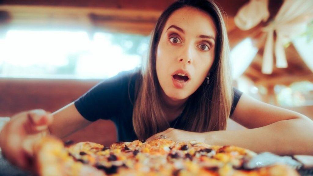 Žena s prekvapeným výrazom sa pozerá na pizzu pred sebou na stole.