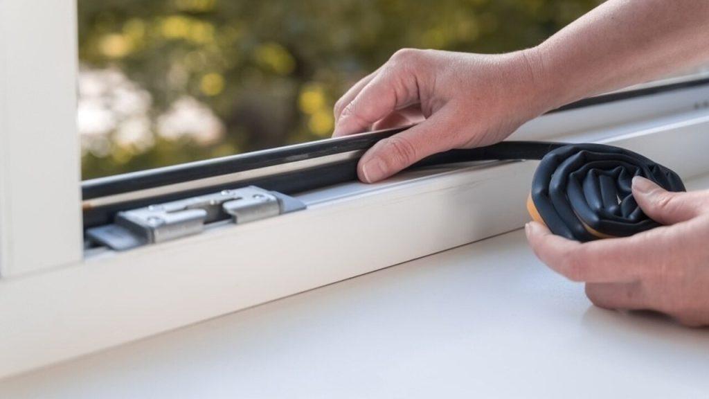 Ruky inštalujú tesnenie na okno pred zimou.