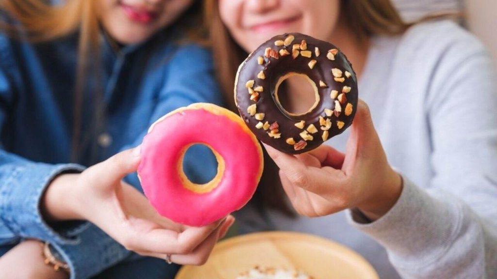 Dve ženy držia farebné šišky – jednu s ružovou polevou a druhú s čokoládovou a orieškami.