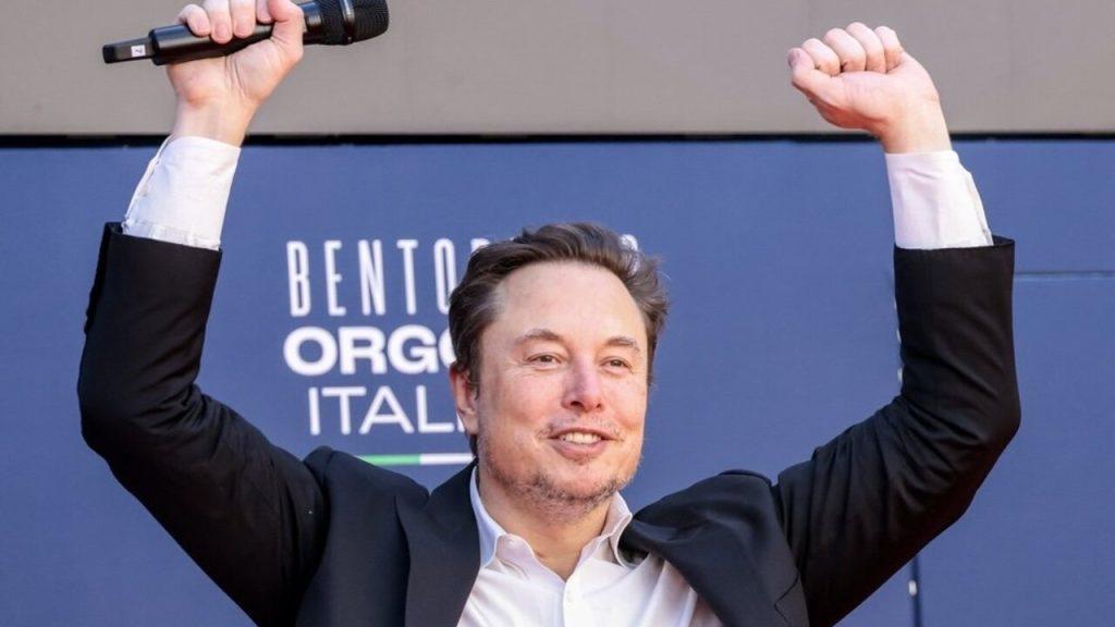 Elon Musk s úsmevom a zdvihnutými rukami počas verejného vystúpenia