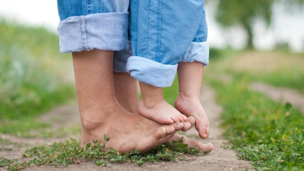 Bosé nohy dieťaťa a rodiča na tráve počas chôdze naboso