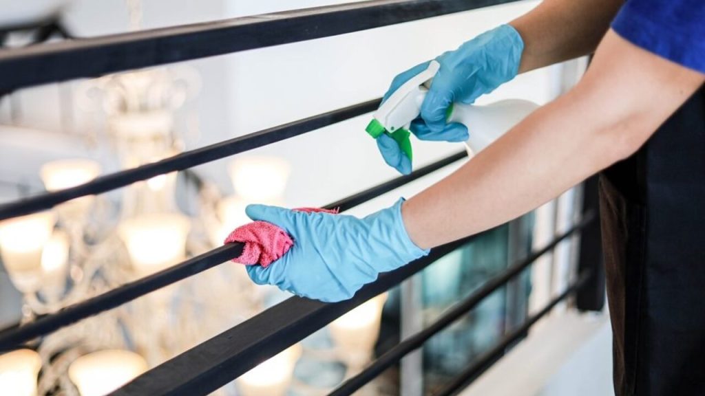 Ruka v rukavici postrekuje zábradlie balkóna čistiacim alebo aromatickým roztokom
