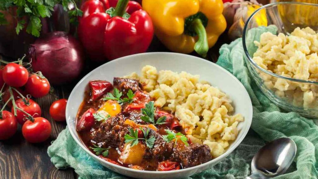 Maďarský guláš podávaný s domácimi haluškami (nokerlami) na tanieri, obklopený čerstvou zeleninou.