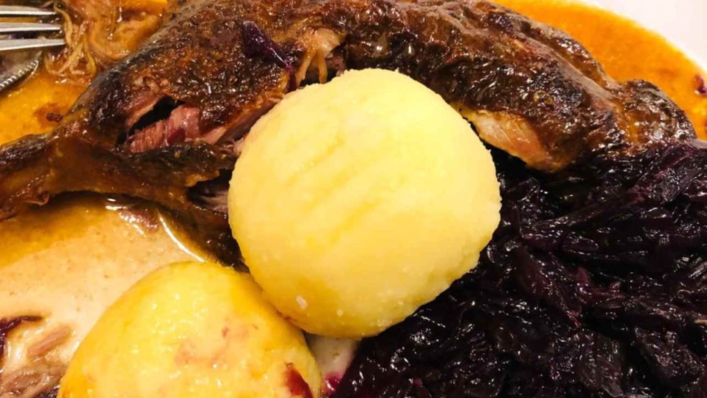 Porcia pečenej husi s červenou kapustou a zemiakovými guľkami na tanieri.