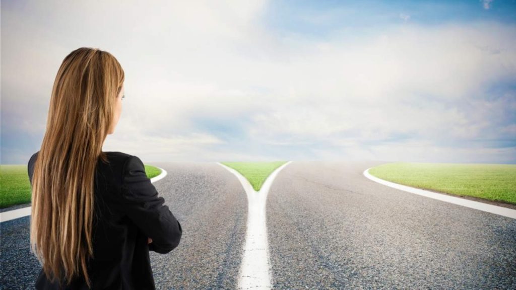 Osoba stojí na križovatke ciest a symbolicky premýšľa o zmene práce.
