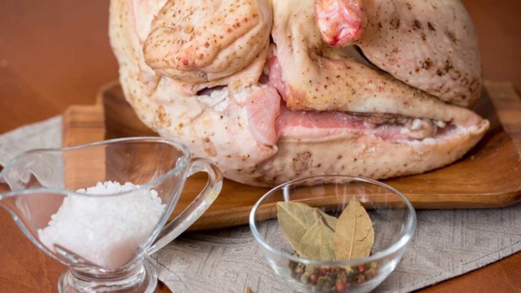Surová hus pripravená na marinovanie, so soľou, bobkovým listom a korením na drevenom lopári.