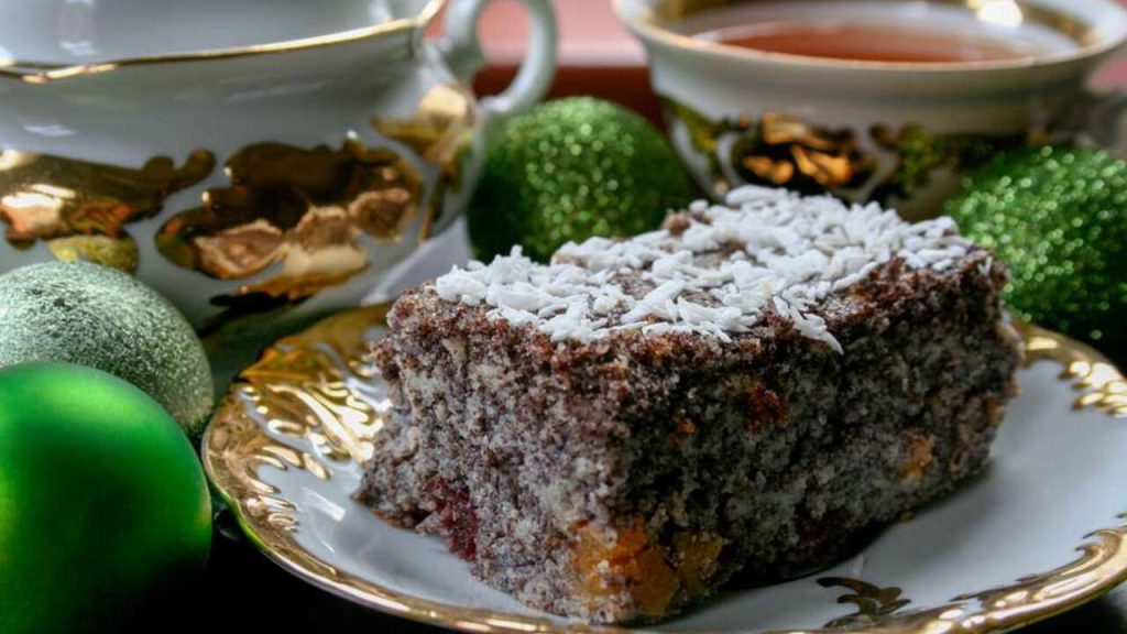 Makový koláč s kokosom na vrchu, podávaný na zlatej porcelánovej tácke v sviatočnej vianočnej atmosfére.