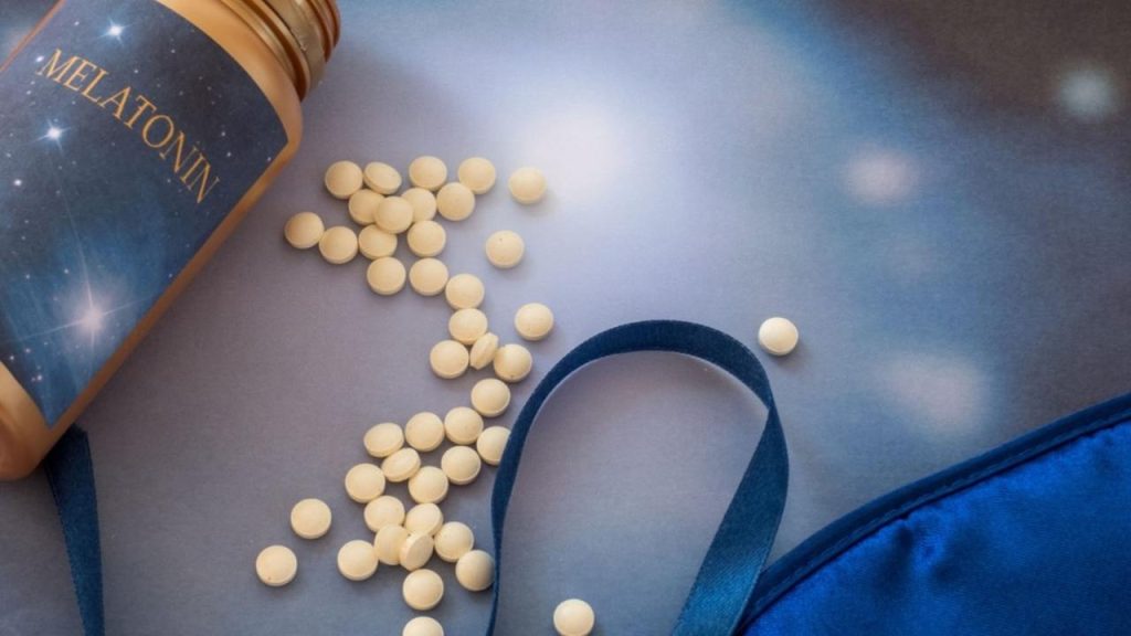 Tablety melatonínu položené na nočnom stolíku vedľa postele.