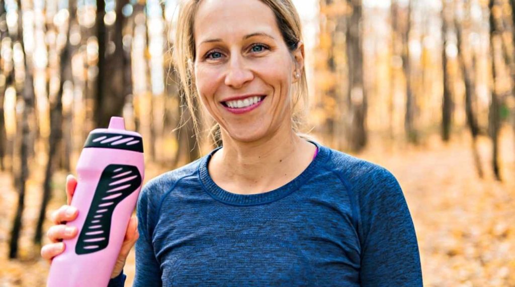 Žena pri prechádzke v lese s ružovou fľašou na vodu v ruke počas jesenného dňa