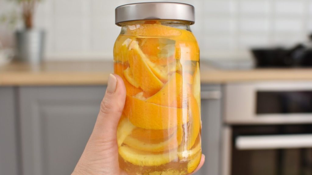 Pohár s pomarančovými šupkami zaliatymi vodou ako domáce hnojivo pre izbové rastliny