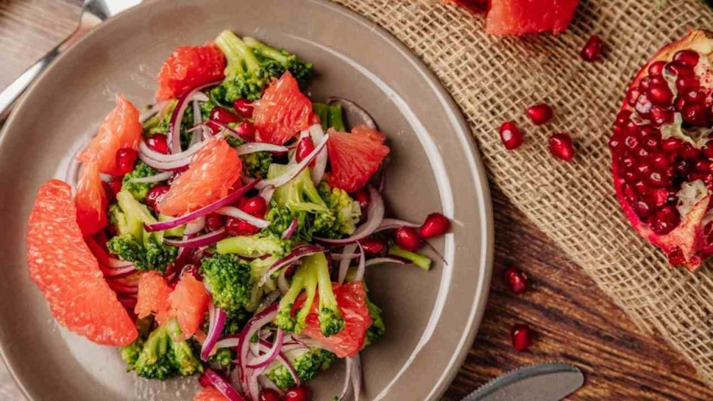 Vegetariánsky šalát s grapefruitom, brokolicou, granátovým jablkom a červenou cibuľou na tanieri.
