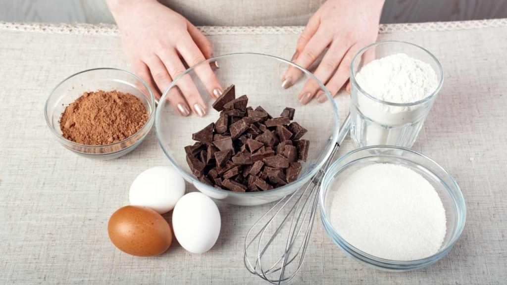 Ingrediencie na prípravu koláča z hrnčeka – kakao, múka, mlieko, maslo a vajce na stole.