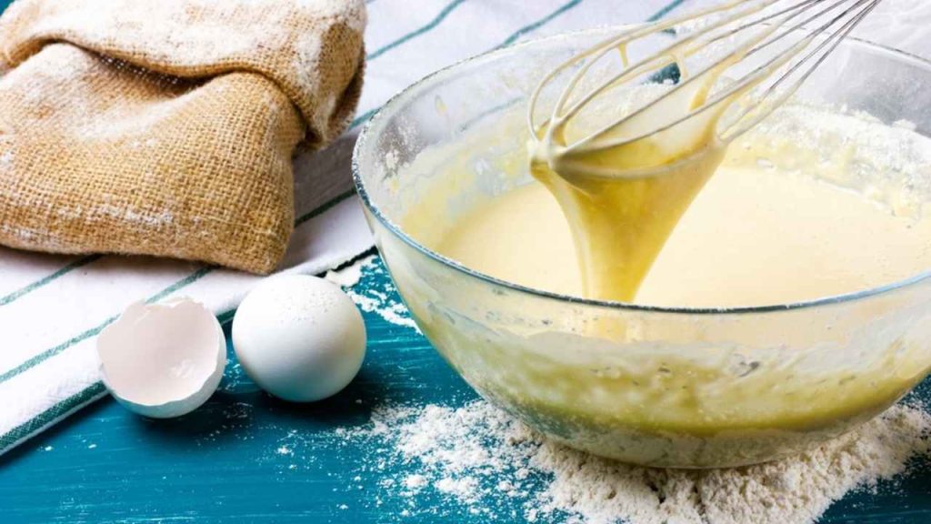 Miešanie cesta na palacinky v miske s metličkou, vajíčkami a múkou