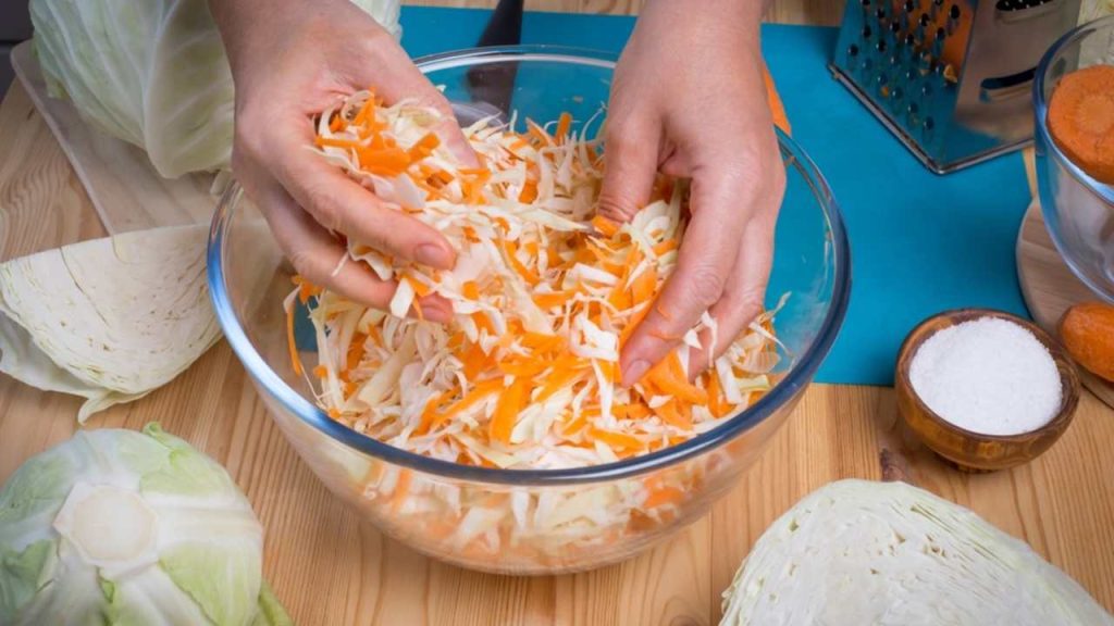 Ruky premiešavajú nastrúhanú kapustu a mrkvu v miske pri príprave čínskeho šalátu.