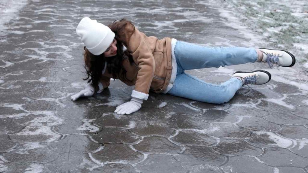 Žena pošmyknutá na zľadovatenom chodníku, ležiaca na boku na klzkom povrchu.