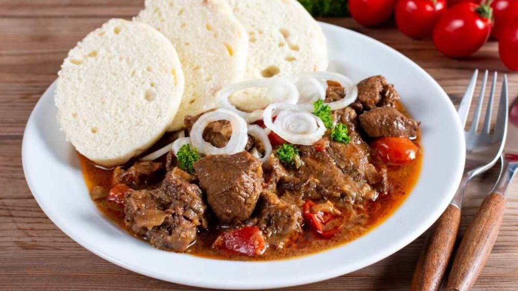 Bravčový guláš podávaný s domácou parenou knedľou na bielom tanieri.