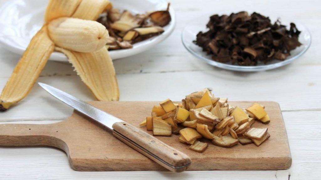 Nakrájané banánové šupky pripravené na prírodné hnojenie, položené na doske spolu s nožom.