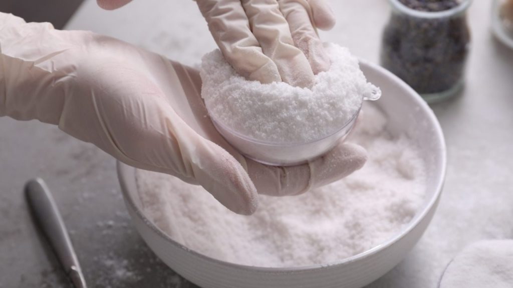 Ruky v rukaviciach tvarujú domácu bieliacu zmes z bieleho prášku v miske.