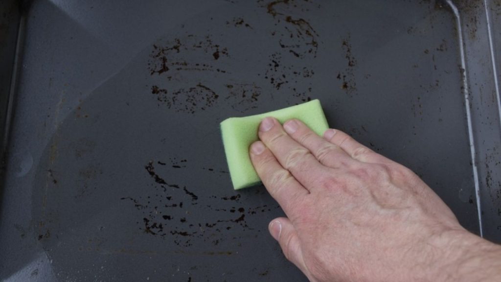 Ruka čistí plech pomocou hubky