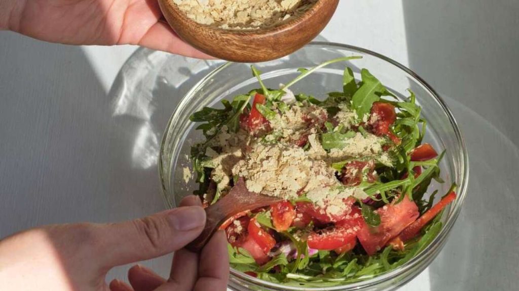 Čerstvý zeleninový šalát posypaný lahôdkovým droždím z drevenej misky.