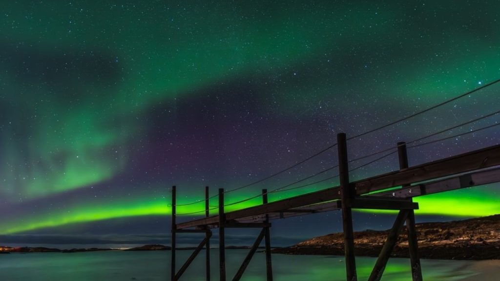 Zimná obloha nad Sommarøy so zelenými vlnami polárnej žiary.