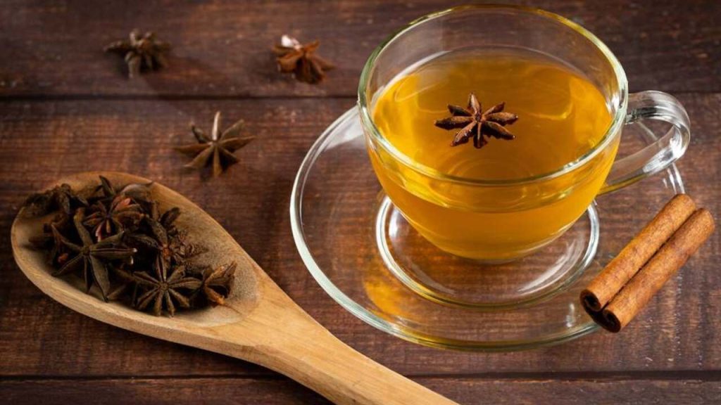 Šálka teplého anízového čaju s hviezdicovým anízom a škoricou na drevenom stole