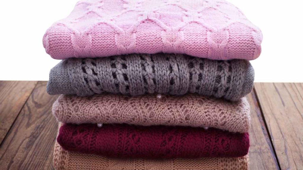 Poskladané vlnené svetre v jemných farbách uložené na drevenom podklade.