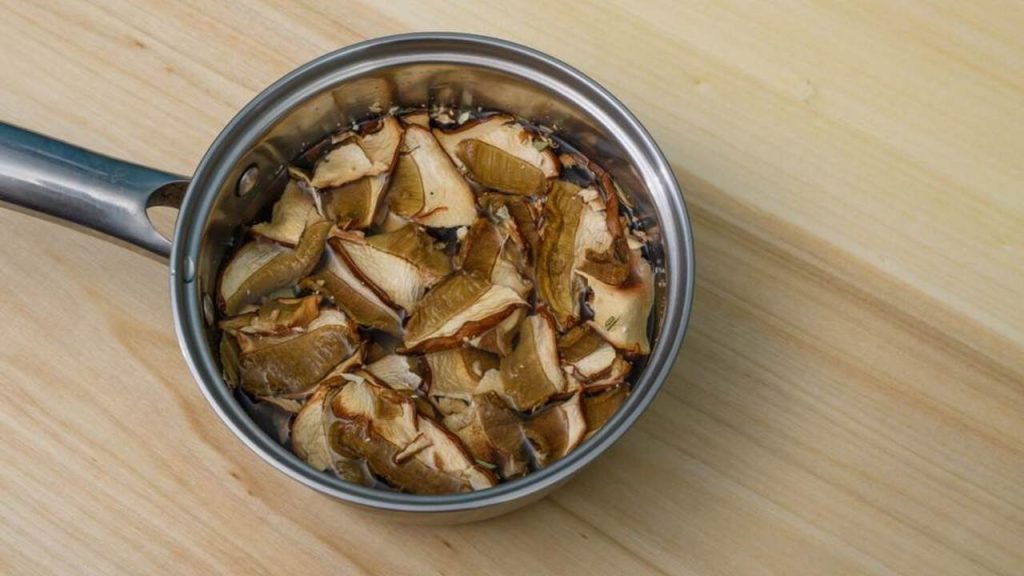 Sušené huby namočené vo vode v malom nerezovom hrnci pripravené na varenie.