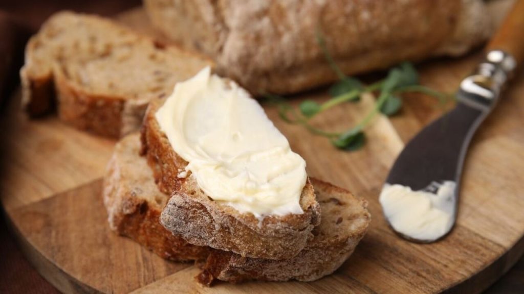 Plátky špaldového chleba natreté maslom na drevenom lopári, pripravené na raňajky.