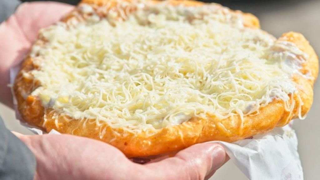 Muž držiaci tradičný maďarský lángos s kyslou smotanou, cesnakom a nastrúhaným syrom.