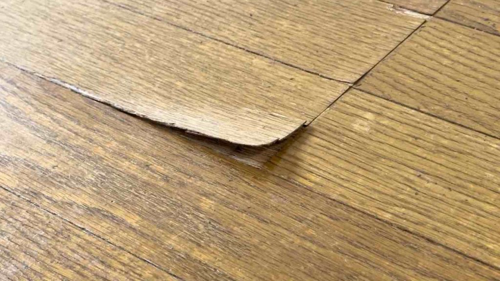 Poškodená laminátová podlaha so zdvihnutým okrajom v dôsledku nadmernej vlhkosti