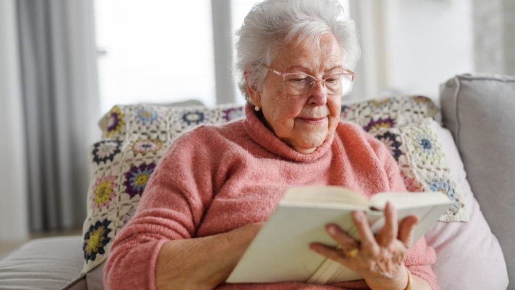 Staršia žena s úsmevom číta knihu ako symbol dobrej pamäti a zdravej mysle