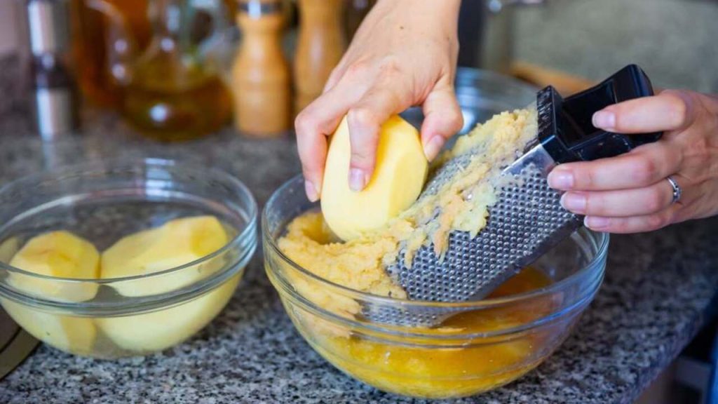 Strúhanie surových žltých zemiakov na jemnom strúhadle pri príprave cesta