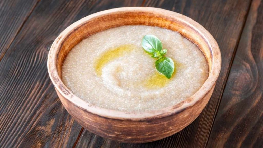 Miska s teplou amarantovou kašou preliatou olivovým olejom, ozdobená lístkami bazalky na drevenom stole.