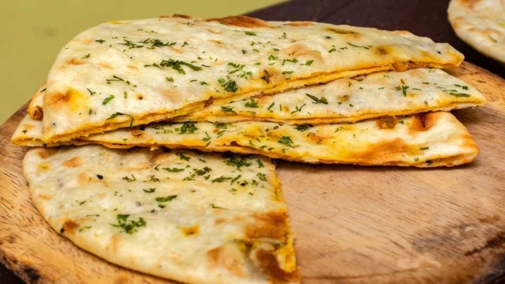 Čerstvo upečený naan potretý maslom a posypaný cesnakom.