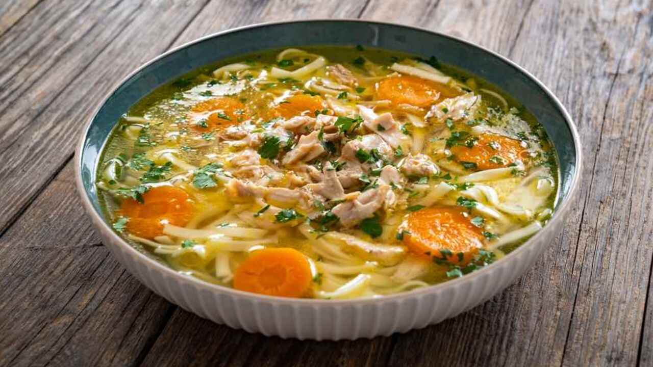 Miska domácej kuracej polievky s rezancami, mrkvou a kúskami mäsa na rustikálnom drevenom stole.