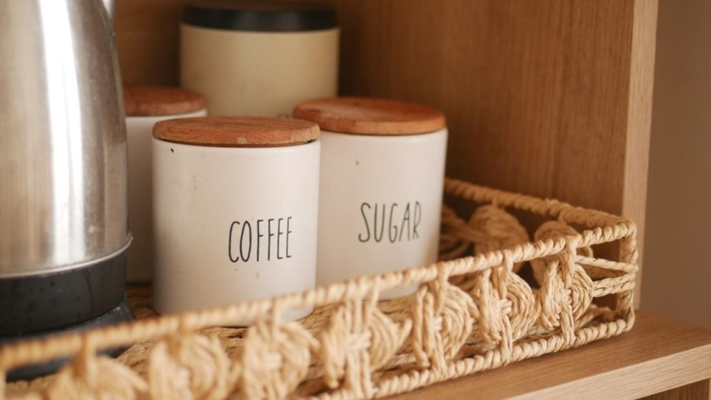 Kávové a cukrové dózy uložené v kuchynskej poličke, vhodné na skladovanie kávy mimo svetla.