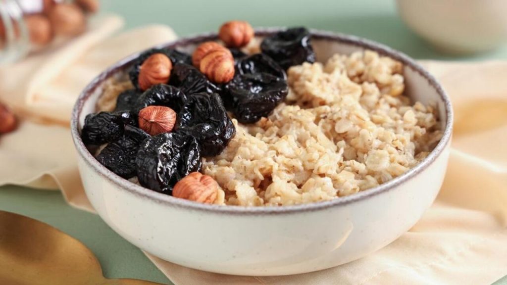 Ovsená kaša podávaná s kúskami sušených sliviek a lieskovými orechmi v miske