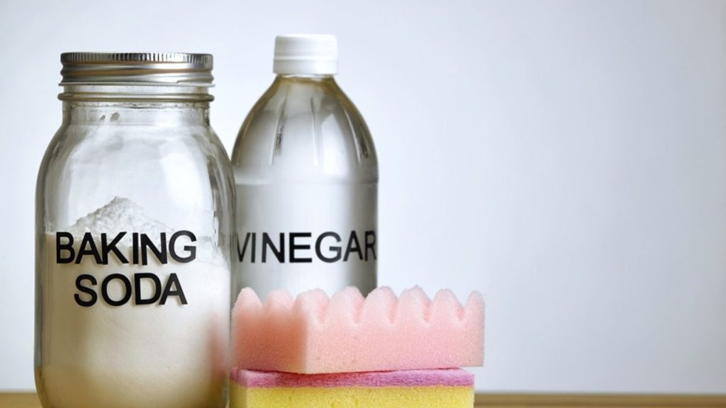 Sklenená nádoba so sódou bikarbónou, fľaša octu a čistiace hubky pripravené na domáce čistenie