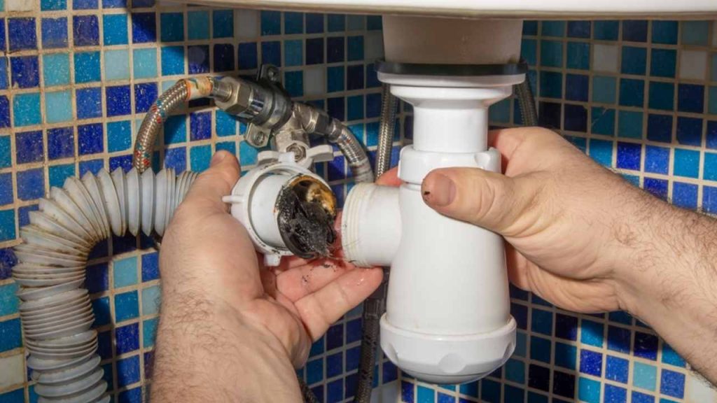 Inštalatér rozoberá sifón pod drezom a odstraňuje z neho nahromadené nečistoty.