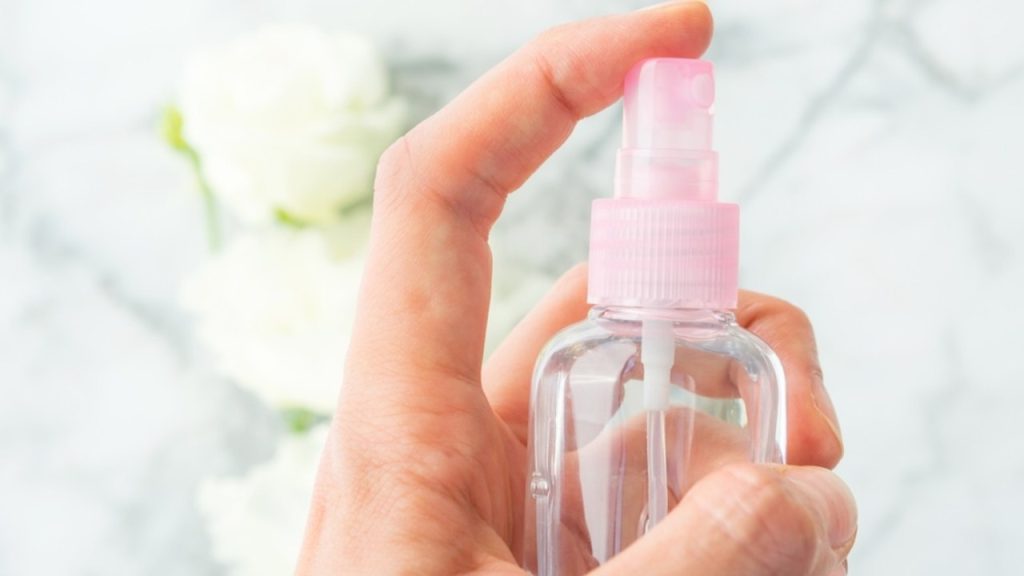 Ruka stláča malý ružový rozprašovač s domácim antistatickým sprejom proti elektrizujúcim vlasom.