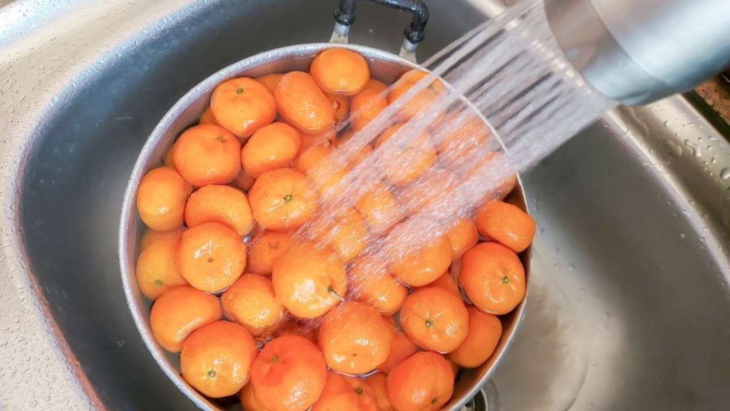 Ruky umývajú mandarínky pod teplou tečúcou vodou pred olúpaním.