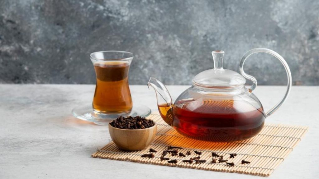 Sklenená kanvica s klinčekovým čajom, pohár teplého nápoja a miska plná klinčekov pripravená na výrobu domáceho kloktadla.