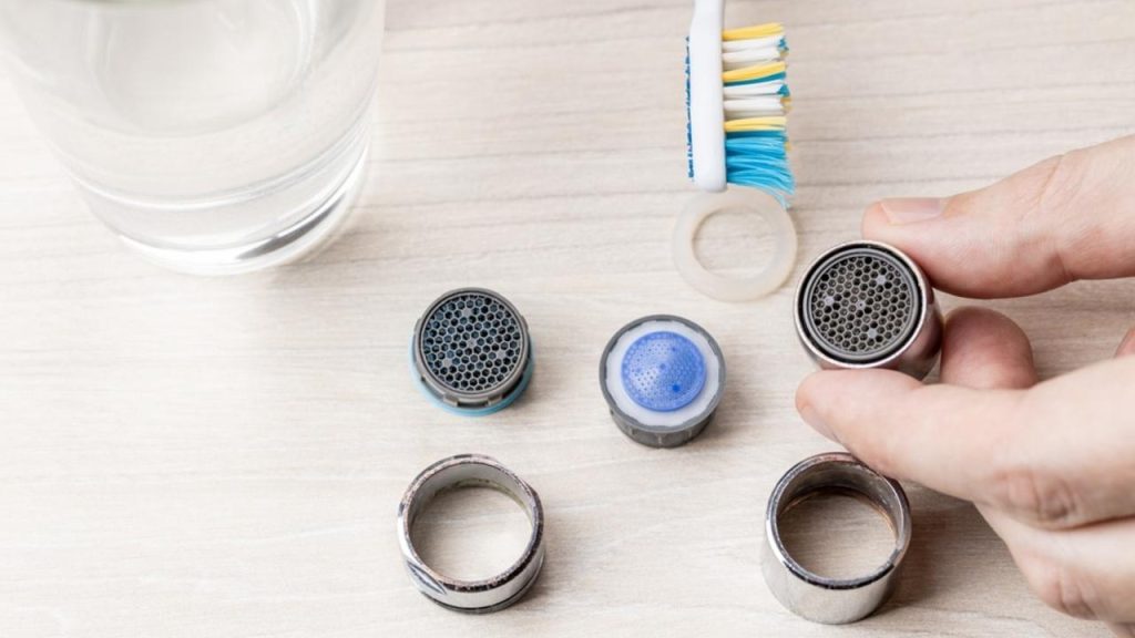 Rozobratý perlátor pripravený na čistenie, položený na stole so zubnou kefkou a pohárom s roztokom.