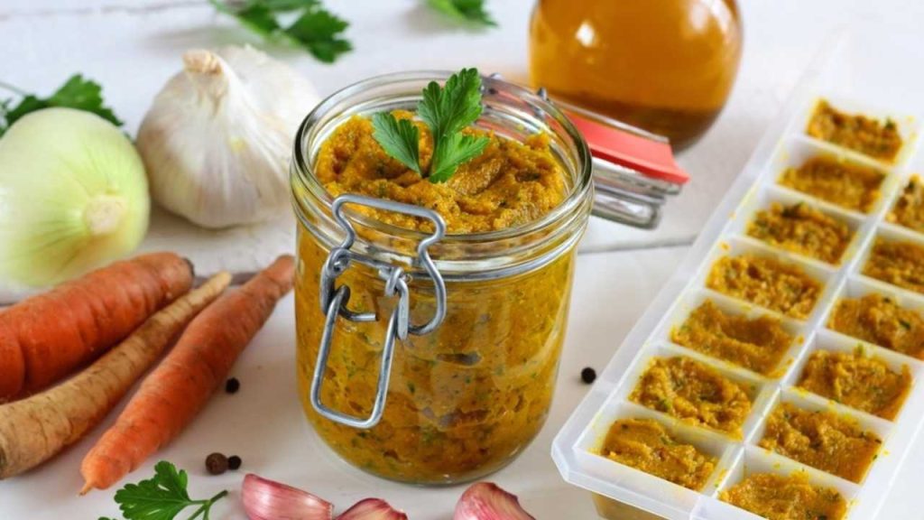 Domáca zeleninová pasta v pohári a v malých dávkach pripravených na zamrazenie, obklopená čerstvou zeleninou.