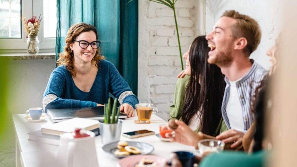 Skupina priateľov pri stole sa smeje a vedie príjemný rozhovor v uvoľnenej atmosfére.