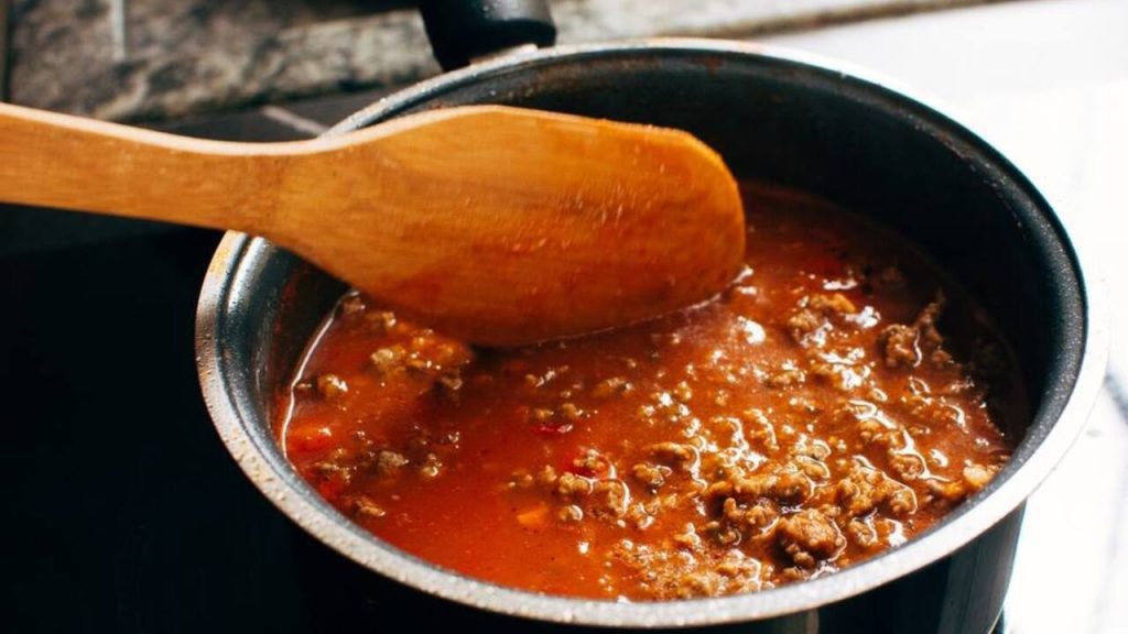 Hustá boloňská omáčka s mletým mäsom pomaly sa variaca v hrnci, miešaná drevenou vareškou.