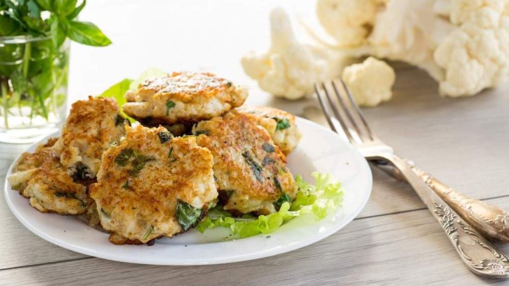 Karfiolové rezne so zemiakmi a bylinkami podávané na bielom tanieri so šalátom